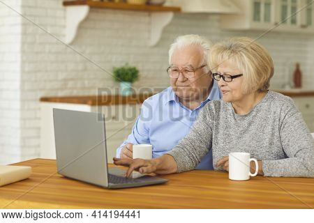 Happy Aged Couple Sitting With Hot Drinks And Watching Movie Or Comminicating Online
