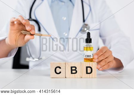 Cropped View Of Doctor Holding Bottle With Cbd And Joint Near Wooden Cubes.