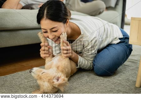 An Asian Woman Playing With Her Dog In The Living Room. Her Family Loves Pets.