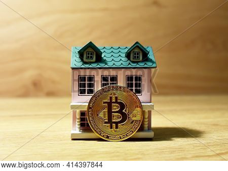 Bitcoin Coin On The Background Of A Wooden House. The Concept Of Buying Real Estate And Housing For 