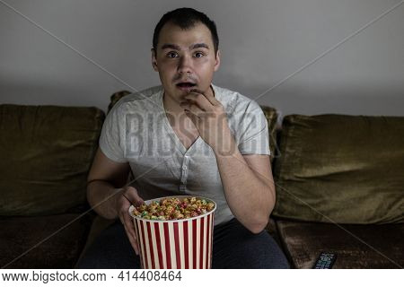 A Man At Home Sitting On The Couch Watching Tv And Eating Popcorn Looks Mesmerized Enjoying A Movie 