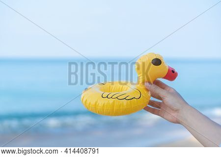 Hand Holding A Yellow Duck On The Beach With A Sea In The Background.