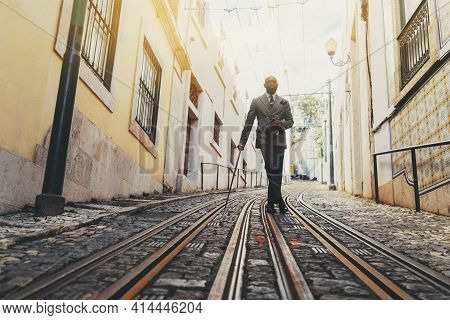 A Dapper Black Senior Man With A Well-groomed Beard And Totally Hairless Is Leaning Against His Fanc