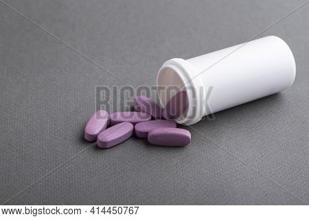 Lilac Medical Pills Are Falling Out Of A White Bottle On A Gray Background. Concept Of Health, Drug 