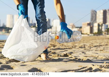 Cleaning Beach From Plastic. Hand Picking Up Plastic Bottle Trash From The Beach And Putting Into Pl