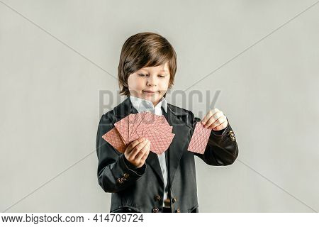 Young Six Year Old Boy Wearing Black Suit And Showing Playing Cards Trick During Illusionist Perform