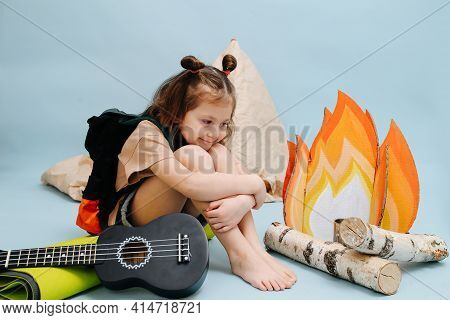 Cozy Little Girl Sitting Next To A Fake Campfire, Hugging Her Knees