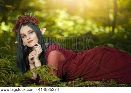 Natural Portrait Of Cute Caucasian Girl In Flowery Garland And Artistic Elf Ears Posing On Ground In
