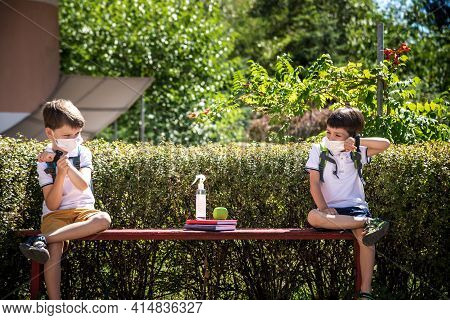 Coronavirus School Reopening Concept: A School Boys Sit On Bench In Front Of A School Wearing A Face
