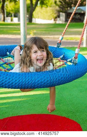Warm summer day in the children's park. Beautiful little girl with long blond hair laughs merrily on a children's swing
