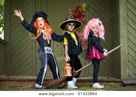 Portrait of three Halloween girls with broom looking at camera outside