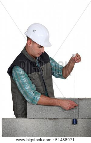Mason checking a wall with a plumb bob.