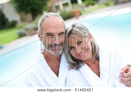 Happy senior couple in bathrobe by resort pool