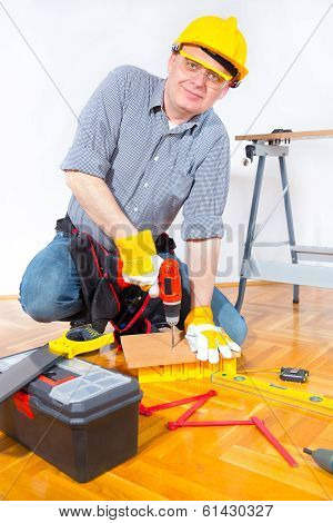 Construction worker holding a drill and drilling wooden board