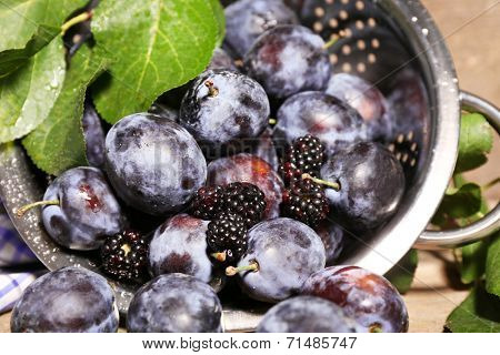 Ripe sweet plums in metal colander, on wooden table