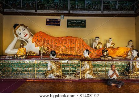 YANGON, MYANMAR - JANUARY 3, 2014: Man meditating near statue of Recumbent Buddha in Shwedagon Paya pagoda