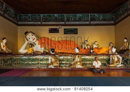 YANGON, MYANMAR - JANUARY 3, 2014: Man meditating near statue of Recumbent Buddha in Shwedagon Paya pagoda