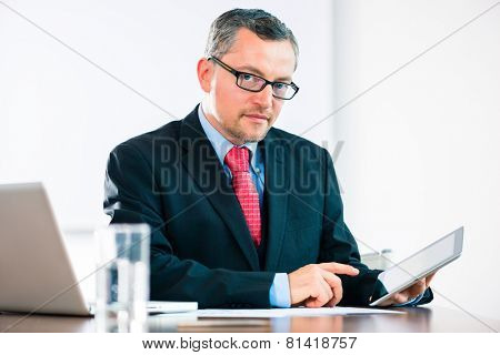 Experienced businessman or lawyer sitting in the Office at desk and working with document or contract on laptop or computer