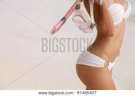 A woman with a beautiful figure near the ocean with snorkeling equipment.