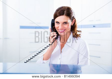 Doctors nurse with telephone in front desk making appointment with patient