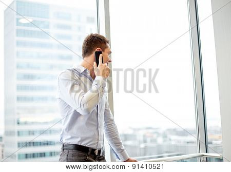 business, technology and people concept - happy businessman calling on smartphone and looking out office window