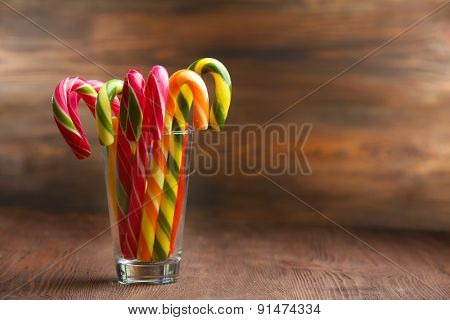 Colorful candy canes in glass on table on wooden background