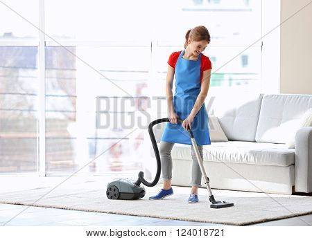 Cleaning concept. Young woman cleaning carpet with vacuum cleaner