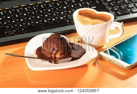Cup of coffee and chocolate cake on heart shaped plate saucer next to laptop notebook computer keyboard and smartphone. Office work desk.
** Note: Visible grain at 100%, best at smaller sizes