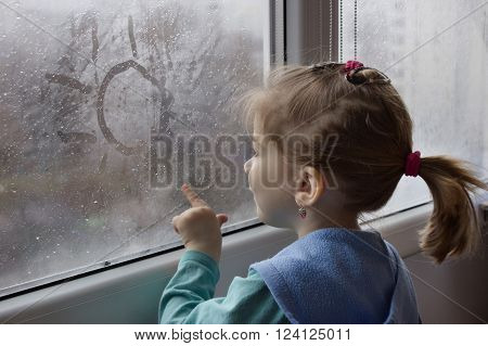 little girl draws a finger the sun on the misted wet glass