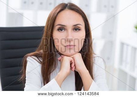 Businesswoman sitting at table head on hands. Ofiice at background. Concept of work.