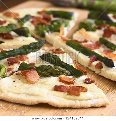 Green asparagus and bacon tarte flambee or Flammkuchen a typical Alsatian and South German dish photographed on wooden board with natural light (Selective Focus Focus one third into the image)