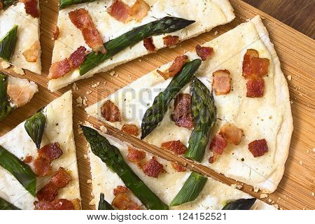 Green asparagus and bacon tarte flambee or Flammkuchen a typical Alsatian and South German dish photographed overhead on wooden board with natural light