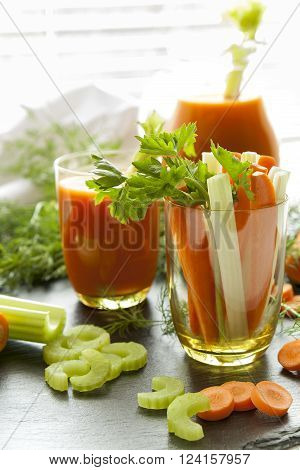 Fresh carrots and celery in glass with fresh carrot juice dill and parsley on black background