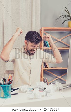 Young man geting angry. A lot of crumpled paper on the table