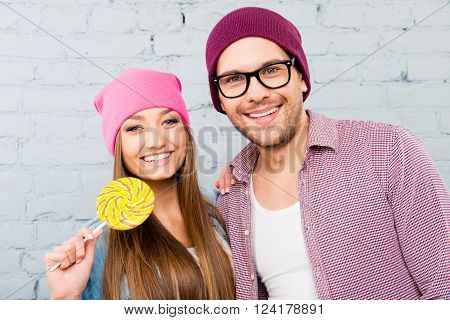 Cute Smiling Man And Woman In Hats And Glasses Holding Lollipop