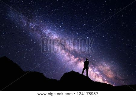 Landscape with Milky Way. Night sky with stars and silhouette of a happy man on the rock. Beautiful Universe. Space background
