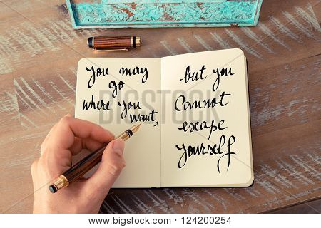 Retro effect and toned image of a woman hand writing on a notebook. Handwritten quote You may go where you want, but you cannot escape yourself as inspirational concept image