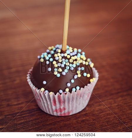 Mini cake on a stick. Chocolate POPCAKE at wrapper on wooden background