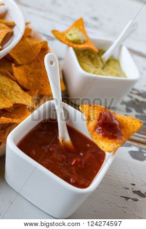 Chili sauce and nachos chips with guacamole sauce on background over an old wooden table