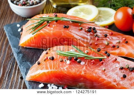 Raw salmon fillet and ingredients for cooking on a slade board and  brown wooden background.