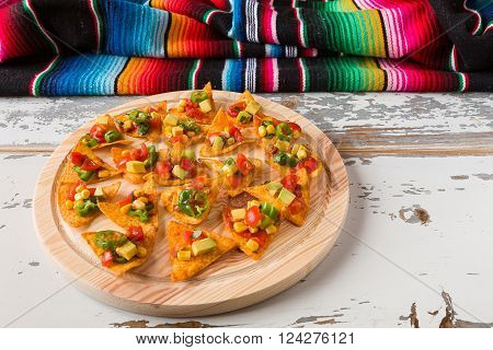 Nachos chips with vegetables on a chopping board and a poncho over an old wooden table