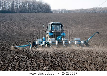 Blue tractor with sower on the field in bright sunny spring morning