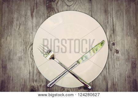 Stop eat concept. Wooden table with empty plate and crossed silver cutlery symbolizing to refuse food. Still life symbolize dieting or unhealthy eating.