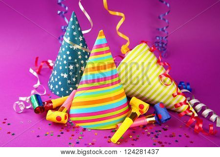 Three Birthday hats with serpentine streamer and noise makers on purple background