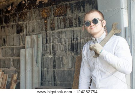 Young mechanic holding big wrench at the old garage