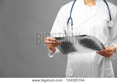 Young female doctor holding radiogram on grey background