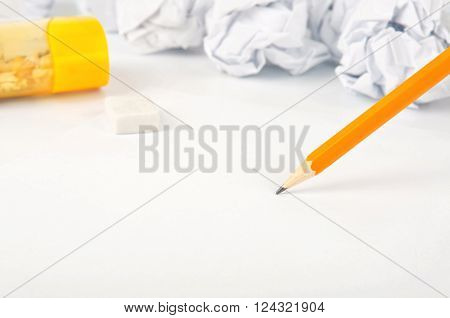 simple pencil on white paper closeup with copy space. In the background is a pencil sharpener eraser and crumpled paper