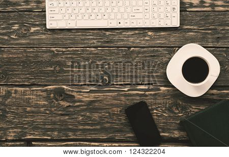 office desktop with a keyboard, a cup of coffee, a smart phone and a notebook, a top view with copy space