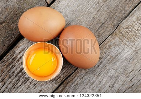 Whole and broken raw brown eggs on wooden table closeup. Top view with copy space