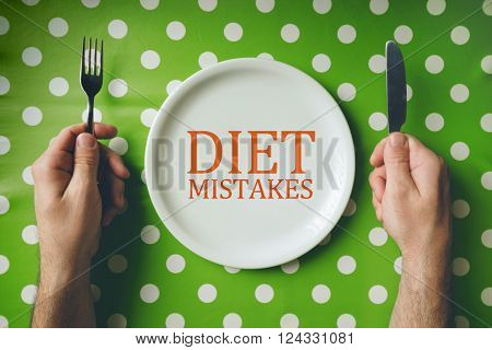 Diet mistakes concept top view of dinning table with male hands holding fork and knife over empty flat plate.